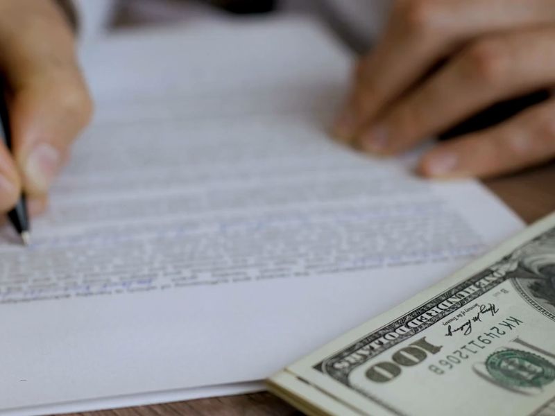 osoba potpisuje papire, pored na papiru stoji novac